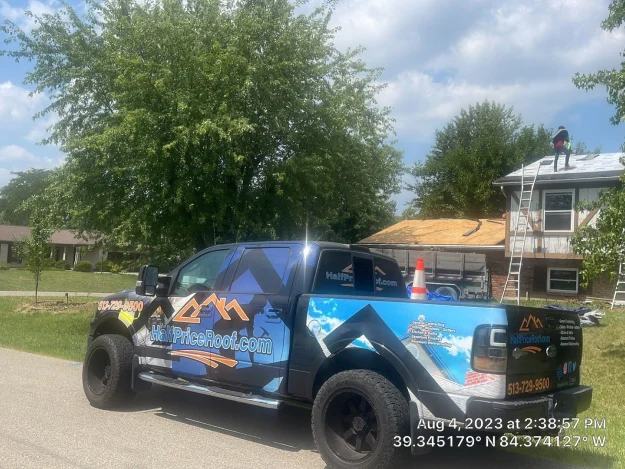 Roofing truck with "Half Price Roof" branding, ladders on a house with a worker, during roof replacement.
